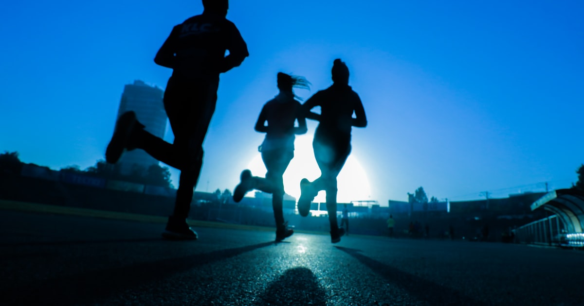 Silhouettes of three people running on a road at dusk