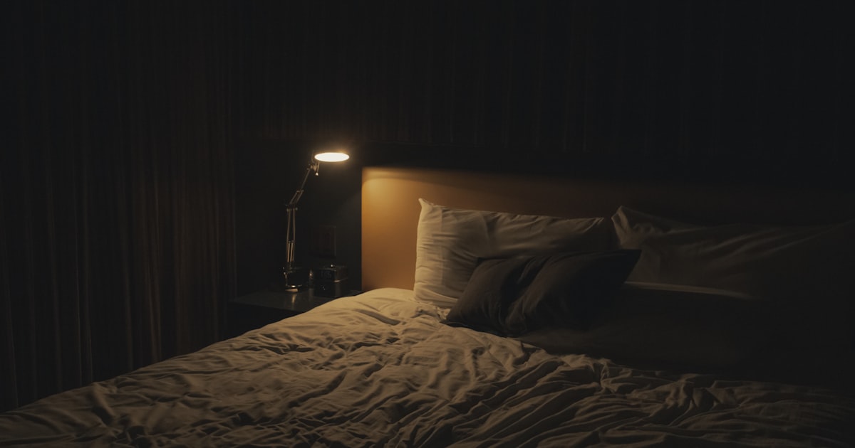 A lit table lamp next to a bed at night