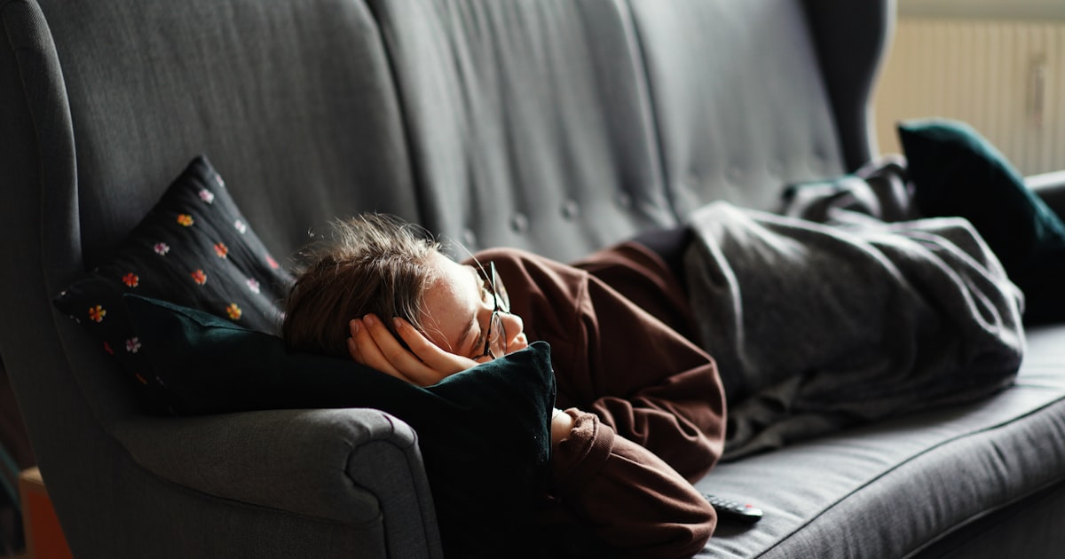 A person napping on a gray couch in the afternoon