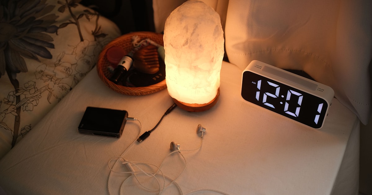 A bedside nightstand with a lamp, a clock, and phone chargers